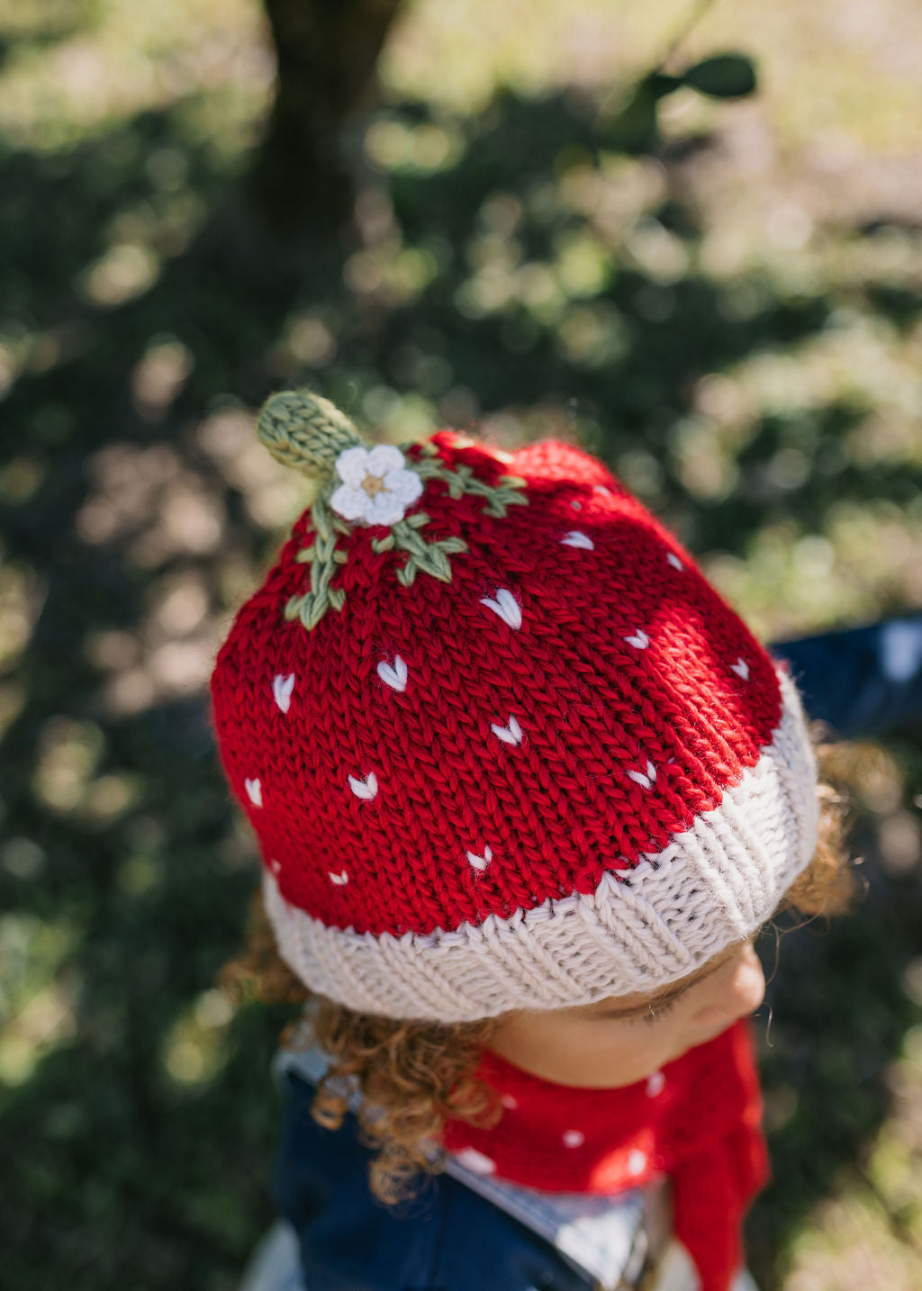 Strawberry Beanie – kids hand-knitted beanie with strawberry, flower, and leaf design in soft wool blend shown on child - top view – Acorn Kids