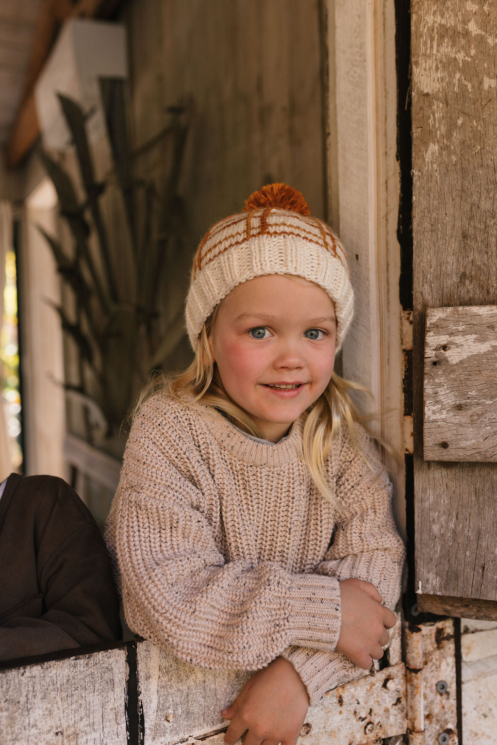 Crossroads Beanie Brown and Caramel on child front view – kids hand-knitted checked beanie with colourful pom pom in soft wool blend – Acorn Kids