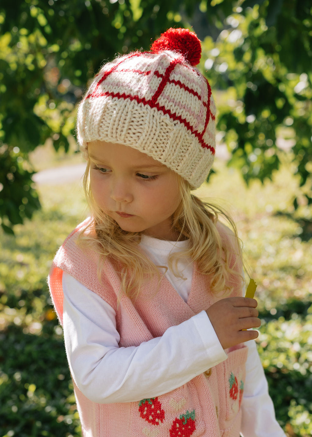 Crossroads Beanie Red and Pink on child front view – kids hand-knitted checked beanie with colourful pom pom in soft wool blend – Acorn Kids