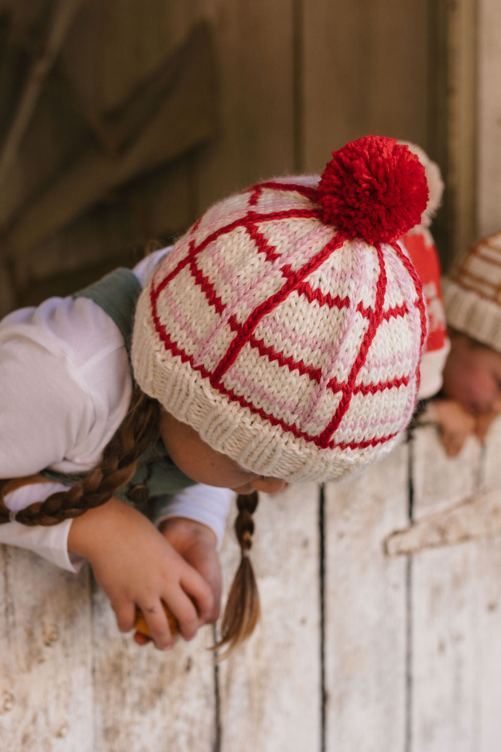 Crossroads Beanie Red and Pink on child close up – kids hand-knitted checked beanie with colourful pom pom in soft wool blend – Acorn Kids
