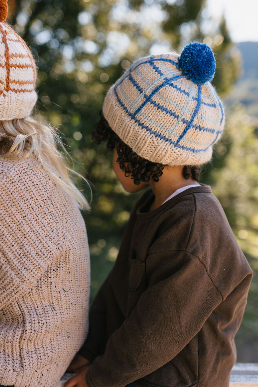 Crossroads Beanie Blue on child side view close up – kids hand-knitted checked beanie with colourful pom pom in soft wool blend – Acorn Kids