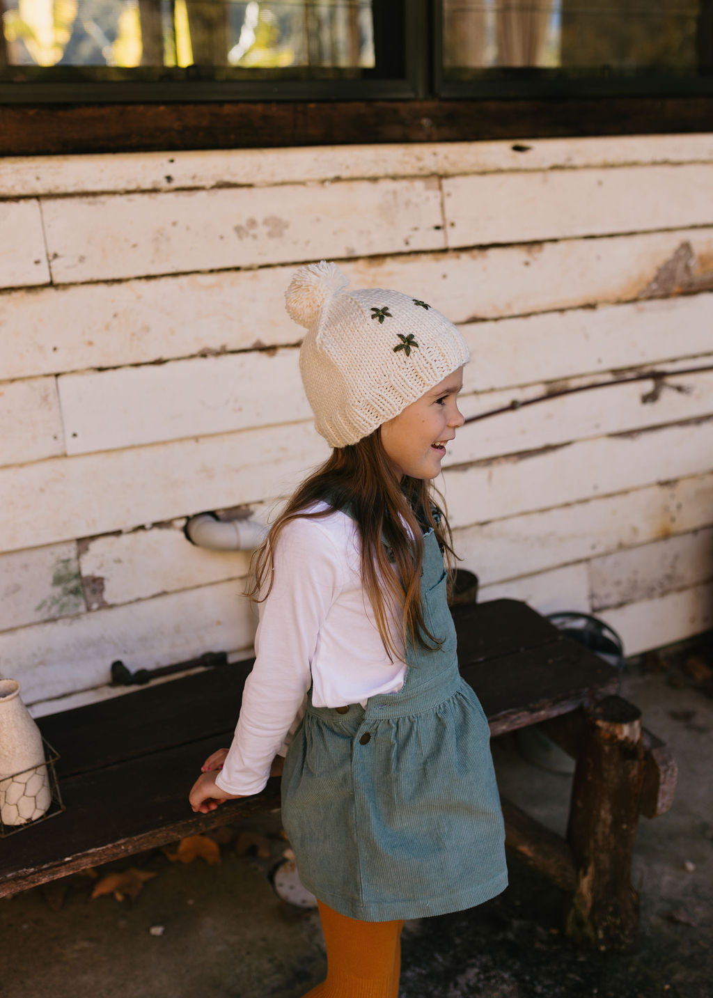 Daisy Beanie – kids hand-knitted beanie with daisy embroidery and pom pom in soft wool blend on child side view – Acorn Kids