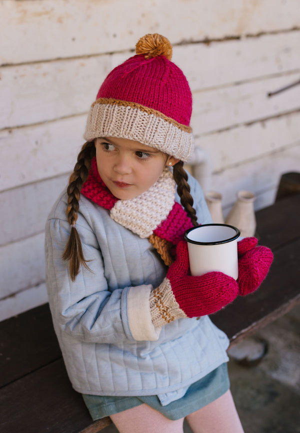 Teddy Beanie and Scarf fuchsia and caramel shown on a child– kids hand-knitted colour block beanie and scarf with pom poms in soft wool blend – Acorn Kids.