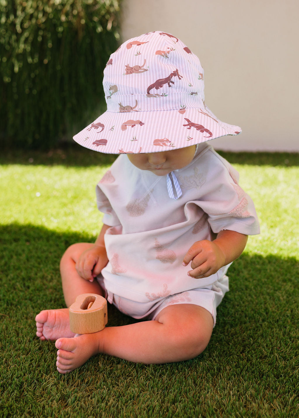 Child wearing Outback Pals Wide Brim Infant Hat sun hat sitting on grass