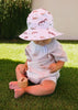Child wearing Outback Pals Wide Brim Infant Hat sun hat sitting on grass