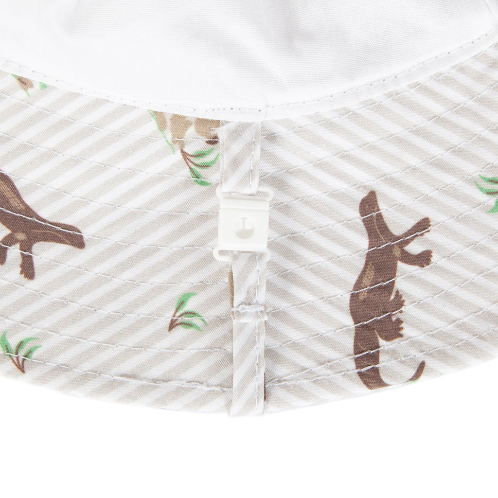 Close-up of a baby hat's interior lining, featuring a white and beige diagonal stripe pattern with brown kangaroo silhouettes and small green leaf accents, secured by a white safety release snap clip.